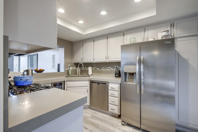 kitchen with a sink, a raised ceiling, appliances with stainless steel finishes, and light countertops