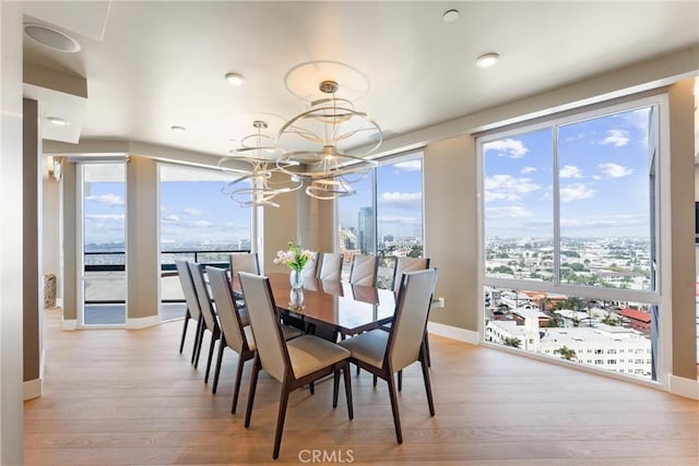 dining space featuring light wood-type flooring, baseboards, a city view, and a chandelier