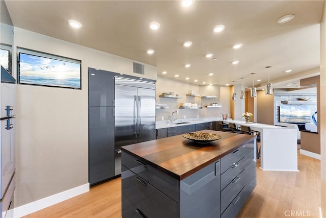 kitchen featuring built in refrigerator, light wood-style flooring, modern cabinets, wood counters, and a sink