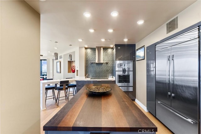 kitchen featuring visible vents, wall chimney range hood, light wood-style flooring, appliances with stainless steel finishes, and modern cabinets