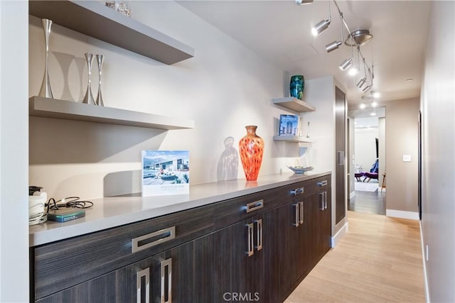 bar featuring baseboards, a bar, rail lighting, and light wood finished floors