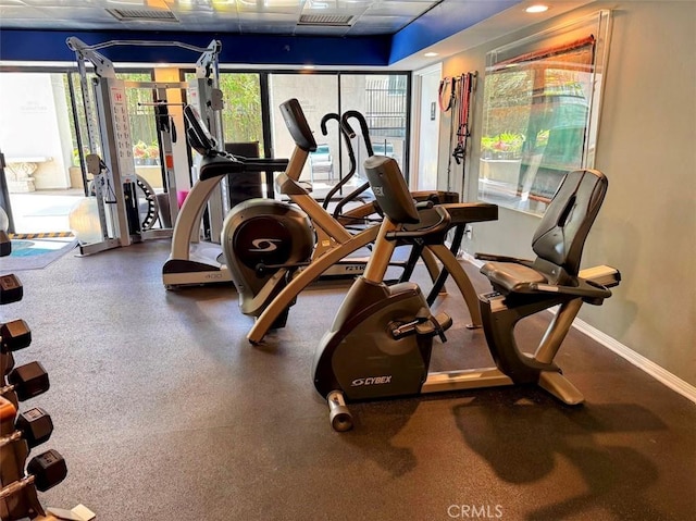 exercise room with visible vents, a paneled ceiling, and baseboards