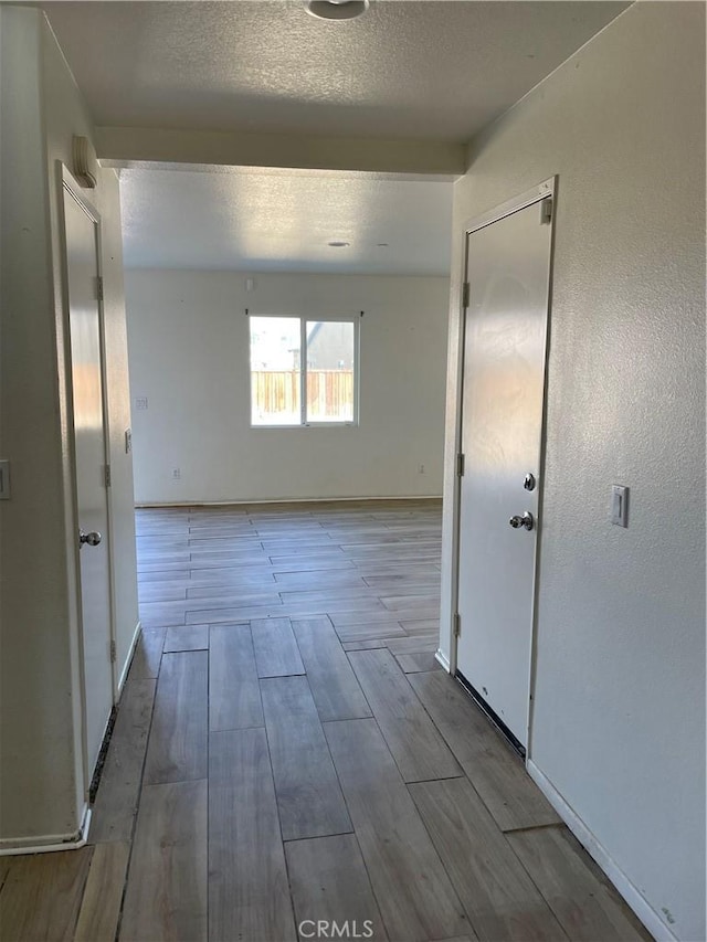 corridor with a textured ceiling, baseboards, and wood tiled floor