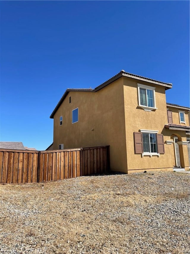 view of home's exterior featuring a tiled roof, stucco siding, and fence