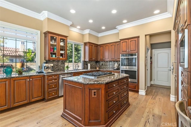 kitchen with backsplash, glass insert cabinets, dark stone counters, appliances with stainless steel finishes, and light wood-style floors