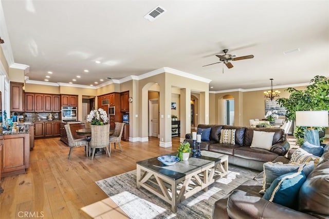 living area featuring visible vents, arched walkways, light wood-style floors, and ceiling fan with notable chandelier