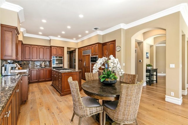 dining area featuring crown molding, arched walkways, visible vents, and light wood-type flooring