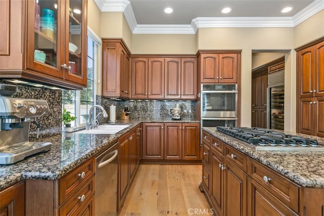 kitchen with ornamental molding, dark stone countertops, a sink, appliances with stainless steel finishes, and glass insert cabinets