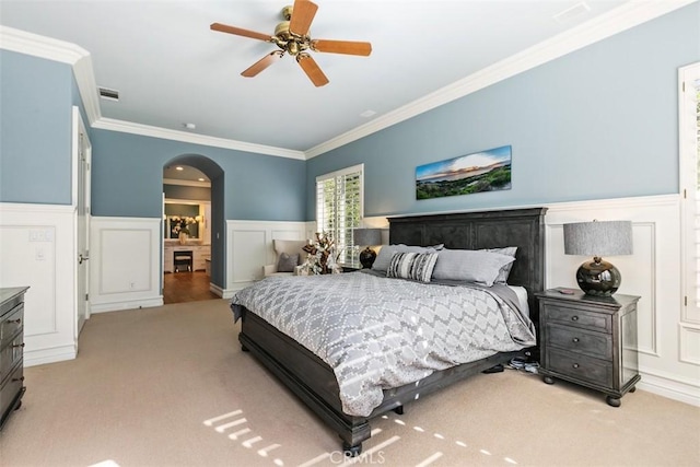 carpeted bedroom with arched walkways, visible vents, crown molding, and a wainscoted wall