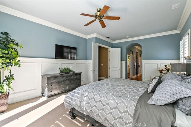 carpeted bedroom with arched walkways, ornamental molding, and wainscoting