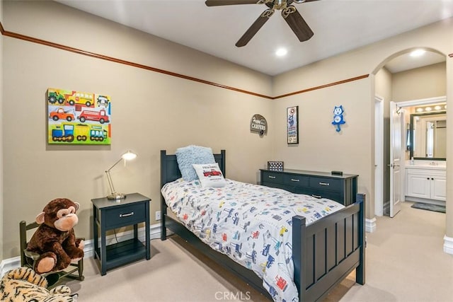 bedroom featuring baseboards, arched walkways, light carpet, and connected bathroom