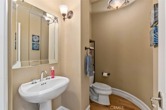 half bath featuring a sink, toilet, baseboards, and wood finished floors