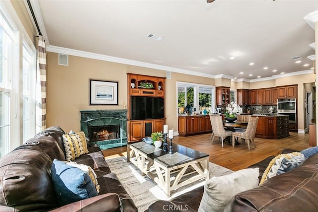 living area with visible vents, light wood-style flooring, and crown molding