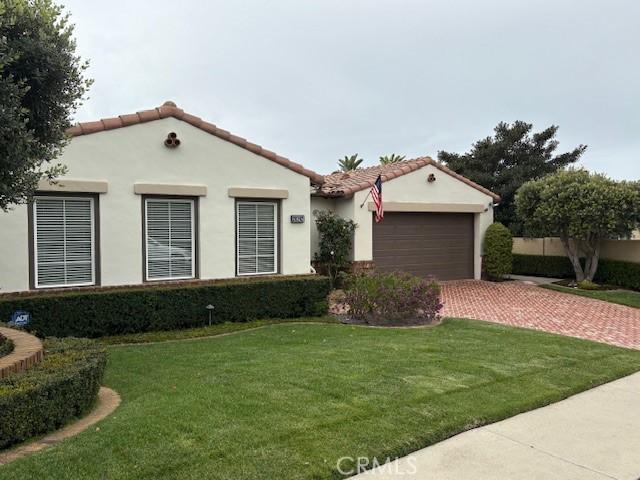 mediterranean / spanish-style home with a front yard, driveway, an attached garage, stucco siding, and a tile roof