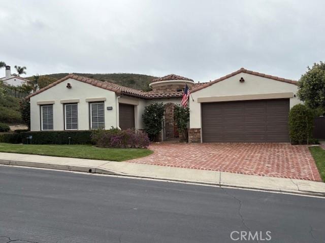 mediterranean / spanish home featuring stucco siding, a front lawn, a garage, a tile roof, and decorative driveway