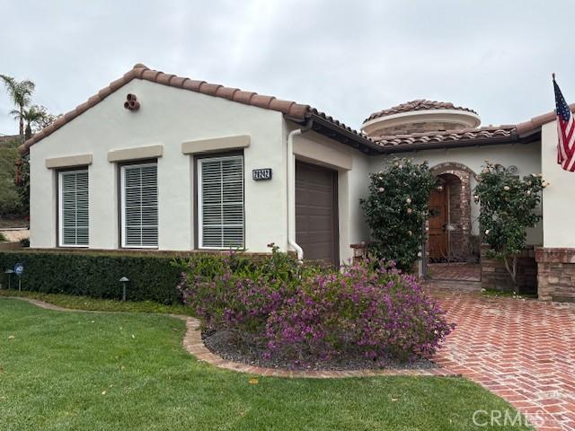 mediterranean / spanish-style home featuring a front yard, a tiled roof, an attached garage, and stucco siding