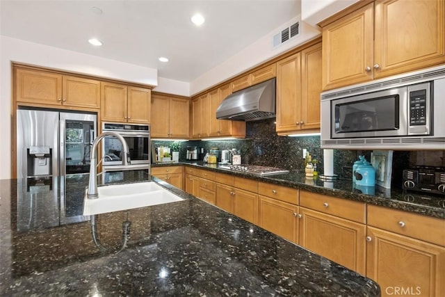 kitchen featuring visible vents, a sink, stainless steel appliances, wall chimney range hood, and backsplash