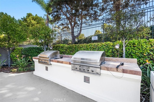 view of patio / terrace featuring exterior kitchen, fence, and a grill