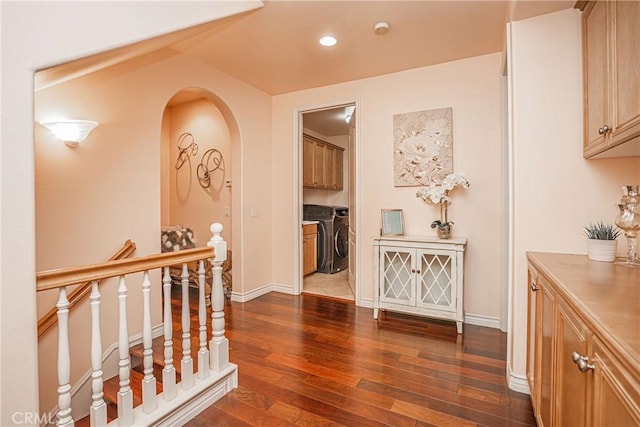 corridor featuring dark wood-style floors, independent washer and dryer, arched walkways, and baseboards