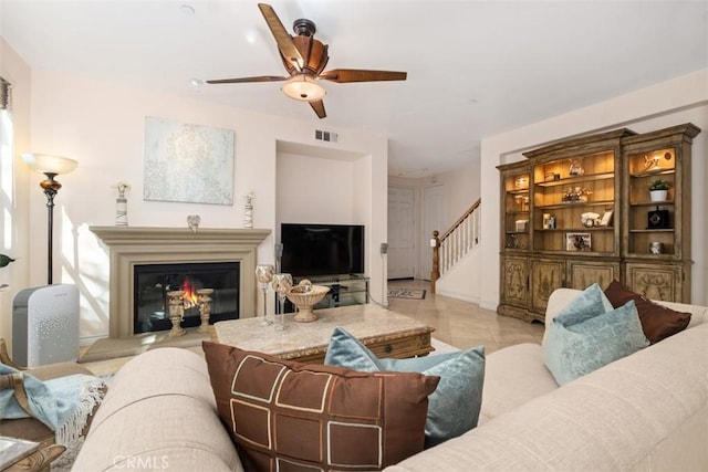 living room featuring visible vents, a glass covered fireplace, a ceiling fan, and stairway