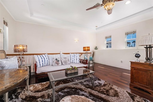 living area with a ceiling fan, a tray ceiling, wood finished floors, and baseboards