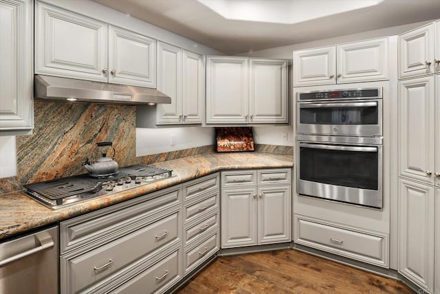 kitchen featuring tasteful backsplash, under cabinet range hood, dark wood finished floors, stainless steel appliances, and white cabinetry