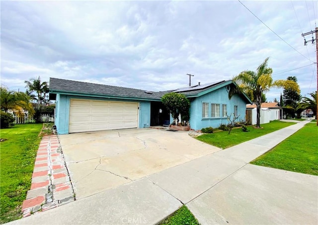 ranch-style home featuring a front yard, driveway, stucco siding, a garage, and roof mounted solar panels