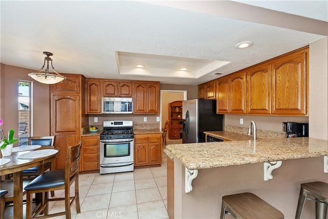 kitchen featuring a breakfast bar area, brown cabinets, a peninsula, stainless steel appliances, and a raised ceiling