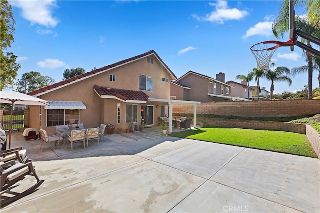 rear view of property with outdoor dining space, fence, a yard, stucco siding, and a tile roof