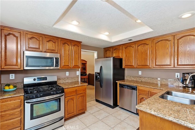 kitchen featuring a sink, stainless steel appliances, a raised ceiling, and a textured ceiling