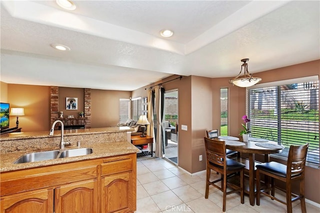 kitchen featuring light stone countertops, light tile patterned flooring, a sink, hanging light fixtures, and open floor plan