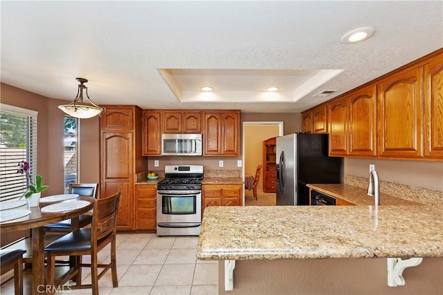 kitchen with a breakfast bar area, a peninsula, appliances with stainless steel finishes, a raised ceiling, and brown cabinets