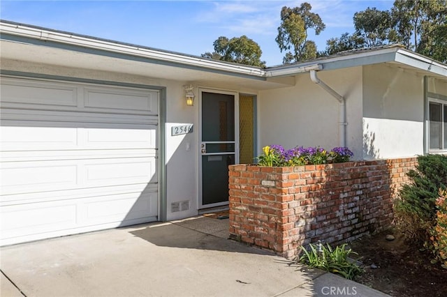 property entrance featuring stucco siding, brick siding, visible vents, and an attached garage