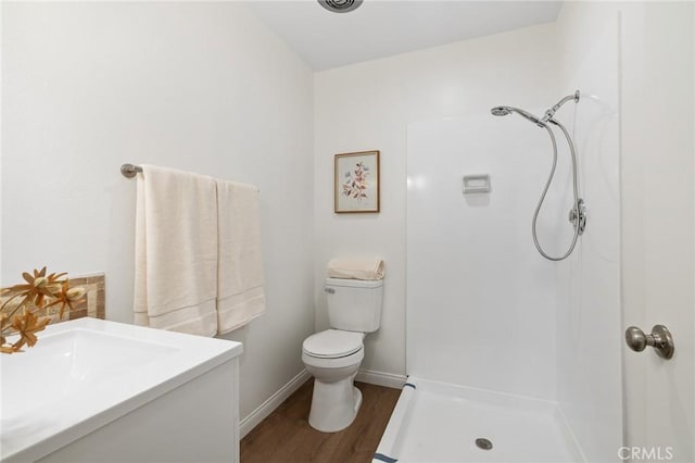 bathroom featuring baseboards, walk in shower, toilet, wood finished floors, and vanity