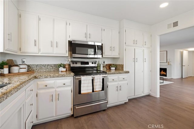 kitchen with visible vents, dark wood-type flooring, white cabinets, appliances with stainless steel finishes, and a brick fireplace