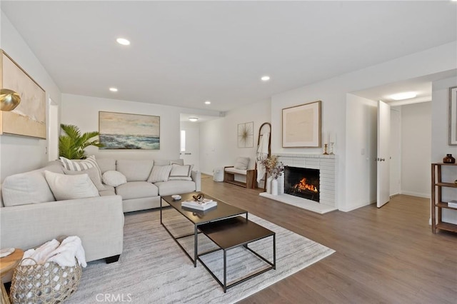 living area featuring a brick fireplace, recessed lighting, baseboards, and light wood finished floors