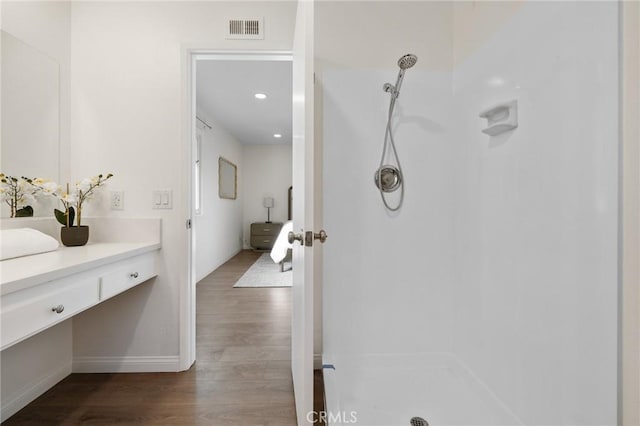 full bathroom with vanity, wood finished floors, a walk in shower, and visible vents