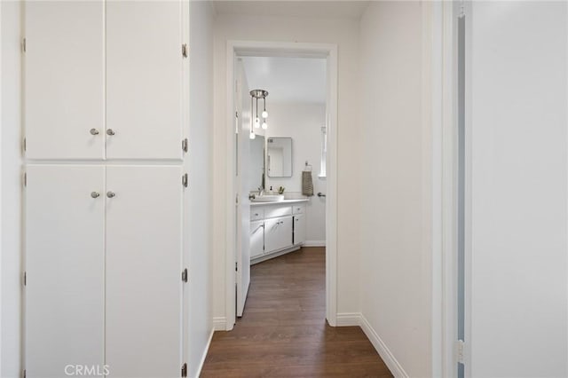 hall featuring dark wood finished floors, baseboards, and a sink