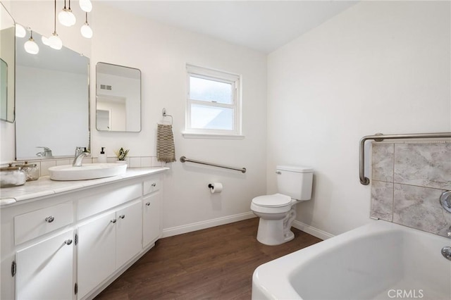 bathroom with vanity, wood finished floors, baseboards, toilet, and a bathtub