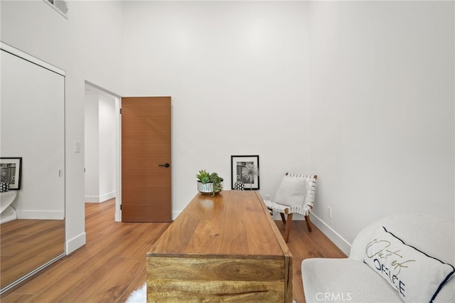 office area with visible vents, wood finished floors, baseboards, and a towering ceiling