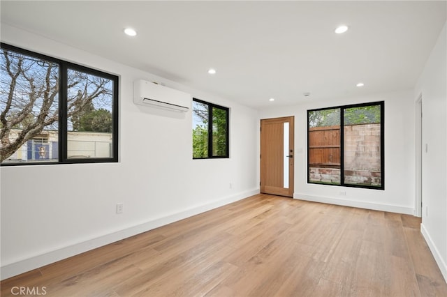 empty room with a wall mounted air conditioner, light wood-type flooring, baseboards, and recessed lighting