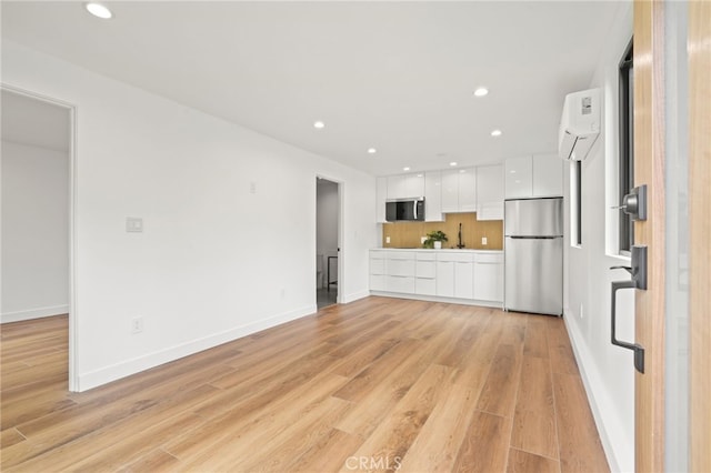 kitchen with light wood-type flooring, modern cabinets, a wall unit AC, appliances with stainless steel finishes, and white cabinets