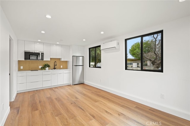 kitchen with a wall mounted air conditioner, decorative backsplash, appliances with stainless steel finishes, white cabinets, and modern cabinets