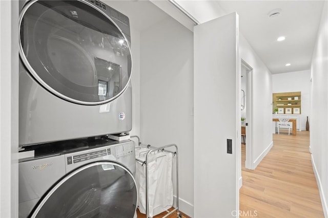 clothes washing area featuring stacked washing maching and dryer, recessed lighting, light wood-style floors, baseboards, and laundry area