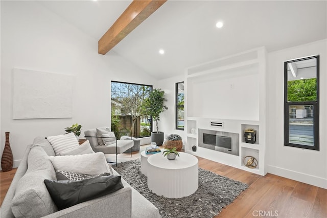 living area featuring a glass covered fireplace, beam ceiling, wood finished floors, and a wealth of natural light