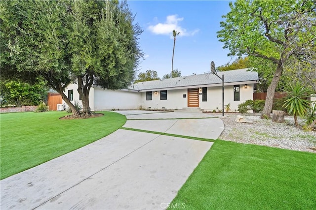 rear view of property with a yard, fence, and stucco siding