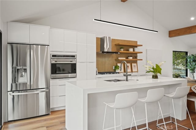 kitchen featuring modern cabinets, a sink, appliances with stainless steel finishes, white cabinets, and wall chimney range hood