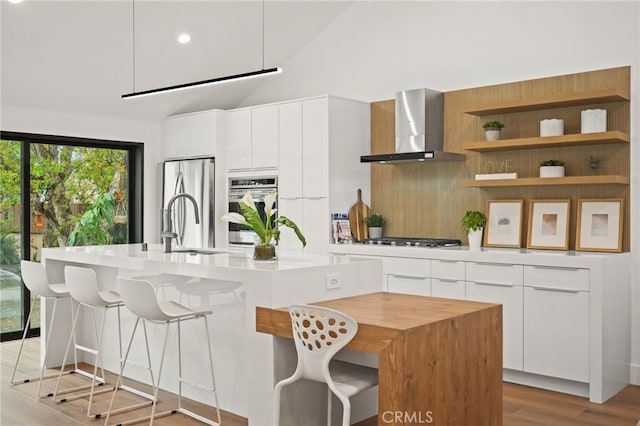 kitchen with a kitchen island with sink, light countertops, appliances with stainless steel finishes, wall chimney exhaust hood, and modern cabinets