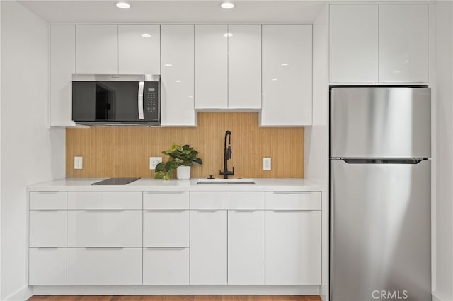 kitchen with a sink, light countertops, appliances with stainless steel finishes, white cabinetry, and modern cabinets