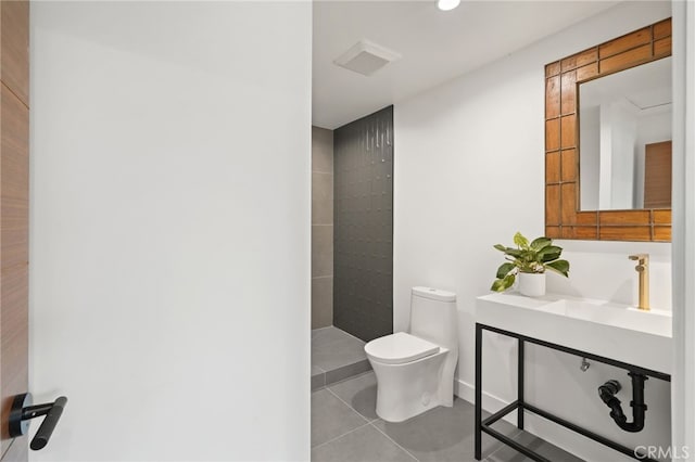 bathroom featuring tile patterned flooring, tiled shower, toilet, and a sink